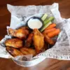 Basket of traditional buffalo wings with bones in, served with celery, carrots and ranch sauce