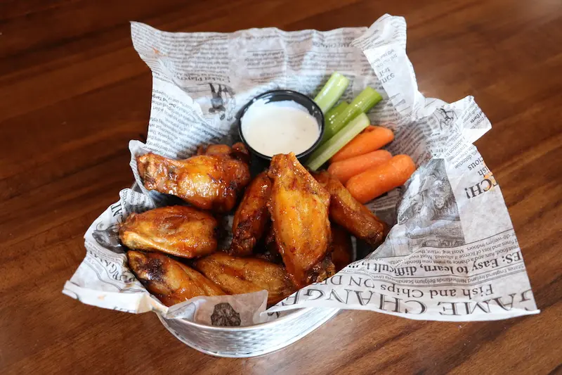 Basket of traditional buffalo wings with bones in, served with celery, carrots and ranch sauce